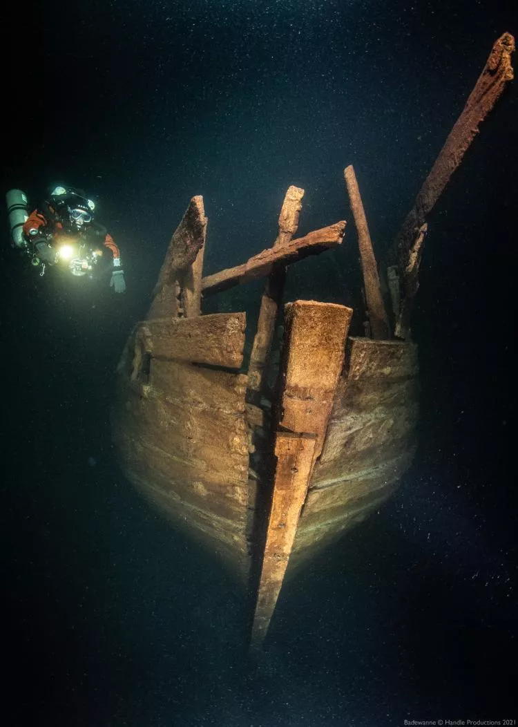 Stern of the wreck. The stern post ends to opening in planking, tiller moved in it. The transom has been above this structure. Uppermost planks on the sides of the stern have fallen away.